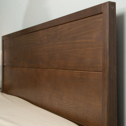 Wooden headboard with a rich brown finish against a light-colored wall.