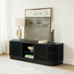 Modern black slatted media console in bright living room with abstract framed painting, sculptural table lamp, black candlesticks and styled books