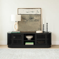 Modern black slatted console table styled with neutral abstract painting, oval ceramic lamp, black candlestick holders, decorative bowl and stacked coffee table books in a minimalist living room