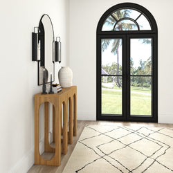 Modern hallway interior with wooden console table, decorative mirror, and elegant arched window overlooking a garden.