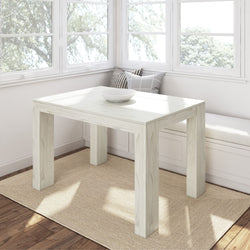 White wooden dining table in a bright sunlit room with cushioned window seating.