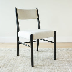 Mid-century modern dining chair with black wooden frame and off-white bouclé upholstered seat and back on a light area rug