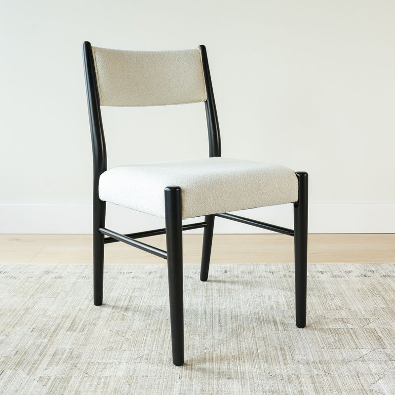 Mid-century modern dining chair with black wooden frame and off-white bouclé upholstered seat and back on a light area rug