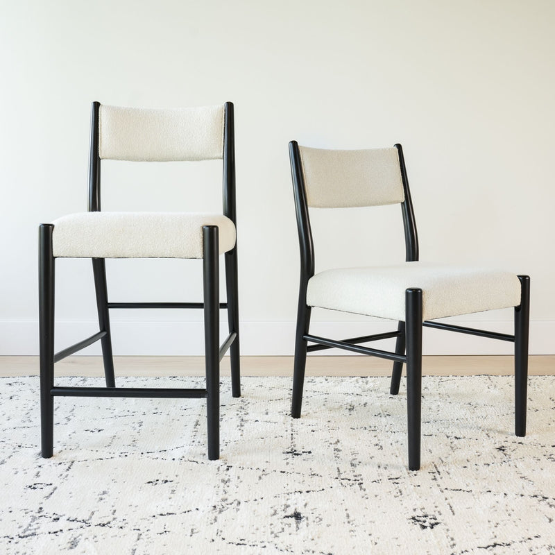 Pair of modern cream upholstered dining chairs with black wooden frames on a patterned cream rug in a minimalist dining room