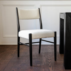 Contemporary dining chair with textured white upholstered seat and back, black wooden frame on dark hardwood floor beside black dining table and white paneled wall