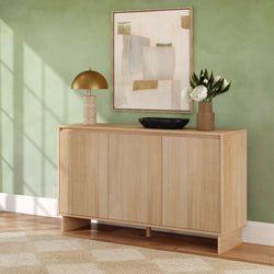 Light oak modern sideboard in a green living room, styled with a gold dome table lamp, abstract wall art, black tray and vase of white flowers