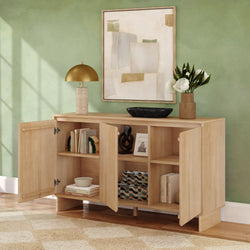 Natural wood modern sideboard with open cabinet doors, storage shelves, brass dome lamp, abstract wall art and vase of white flowers against a green wall