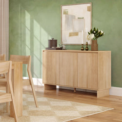 Light wood sideboard and dining chairs in a modern dining room with a green accent wall, abstract wall art, decorative vases, natural sunlight and hardwood floor