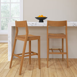 Wooden bar stools at a marble kitchen island with a bowl of oranges, wooden flooring, and a large window.
