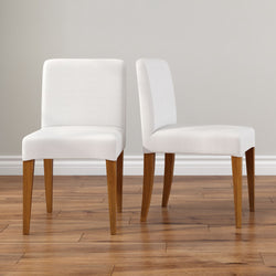 Pair of modern white upholstered dining chairs with wooden legs on hardwood floor against a neutral wall