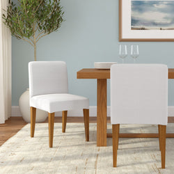Upholstered white dining chairs with tapered wooden legs beside a mid-century modern oak dining table on a neutral area rug