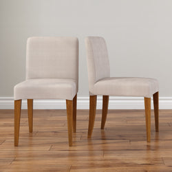 Pair of beige upholstered dining chairs with wooden legs on hardwood floor against neutral wall