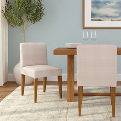 Beige upholstered dining chairs with wooden legs paired with a mid-century wooden dining table in a light-blue dining room with neutral area rug and potted plant