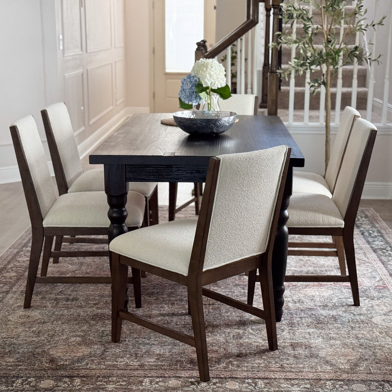 Modern farmhouse dark wood dining table 6-seater with cream upholstered chairs, centerpiece on rug in neutral dining room