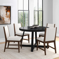 Modern round black dining table with four white upholstered wooden chairs in a bright minimalist dining room with large windows and abstract wall art.