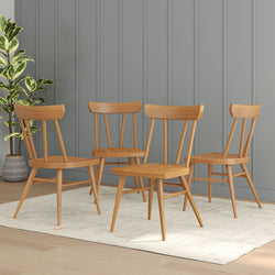 Four mid-century modern wooden dining chairs on a light rug with a potted plant and gray paneled wall background.
