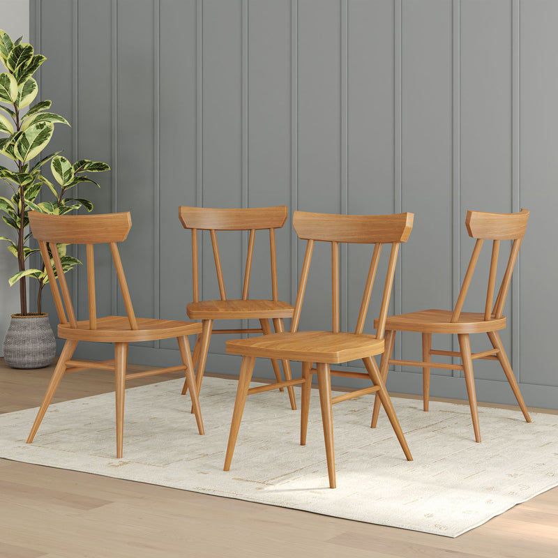 Four mid-century modern wooden dining chairs on a light rug with a potted plant and gray paneled wall background.