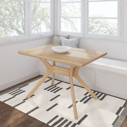 Modern wooden dining table with geometric design and decorative bowl, set in a bright, cozy room with large windows and bench seating.