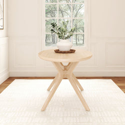 Round wooden table with modern design and potted plant centerpiece in a bright, minimalist dining room.