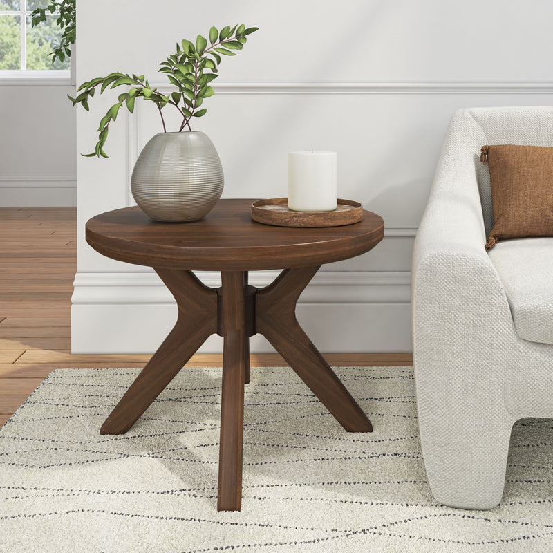 Round wooden side table with vase and candle in modern living room decor.