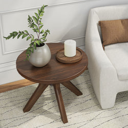 Modern wooden side table with plant and candle next to beige sofa in cozy living room setting.