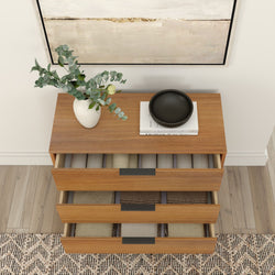 Top-down view of a modern wooden dresser with three open drawers neatly organizing folded linens, white vase with eucalyptus and yellow rose, black decorative bowl on stacked books, hardwood floor and patterned rug, contemporary entryway storage and home decor