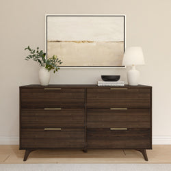 Mid-century modern dark wood six-drawer dresser with brass handles, table lamp, vase of eucalyptus and abstract wall art in a neutral living room
