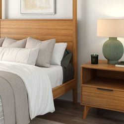 Mid-century modern bedroom with wooden bed frame, neutral linen bedding and beige pillows, knit gray throw, and wooden nightstand with green ceramic lamp and scented candle