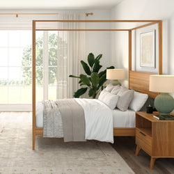 Sunlit modern master bedroom with wooden four-poster bed, neutral linens, large window with sheer curtains, mid-century nightstand, table lamps and potted green plant