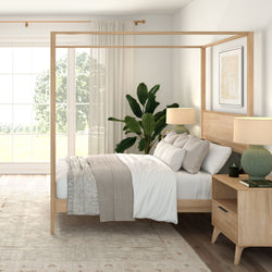 Modern neutral bedroom interior with wooden four-poster canopy bed, white bedding and beige throw, matching nightstands with green table lamps, large window with sheer curtains, indoor potted plant and natural light