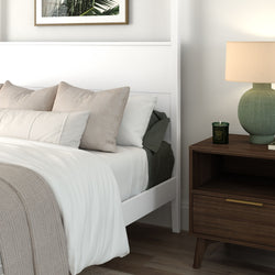 Cozy modern bedroom with white bed frame, neutral bedding and beige pillows, wooden nightstand with green lamp and scented candle
