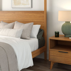 Cozy modern bedroom with mid-century wooden bed frame, crisp white bedding and beige pillows, wooden nightstand with green ceramic lamp and scented candle, neutral minimalist decor