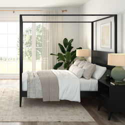 Modern bedroom with black four-poster canopy bed, neutral linen bedding, bedside lamps, large window and indoor plant