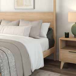 Minimalist modern bedroom with light wood bed frame, neutral white and beige bedding, textured knit throw and wood nightstand with lamp and candle