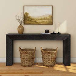 Black wood entryway console table with two woven wicker baskets, ceramic vase with branches, framed landscape print and candles on hardwood floor