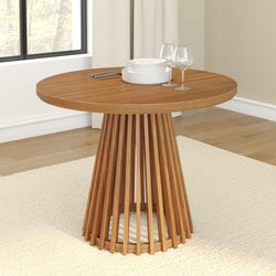 Modern wooden round dining table with decorative pedestal base, set with white plates and wine glasses on a light beige rug.