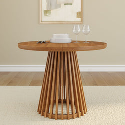 Round wooden dining table with modern base design, set with plates and wine glasses in a minimalist dining room.