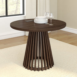 Round wooden dining table with modern pedestal base in a bright dining room setting.