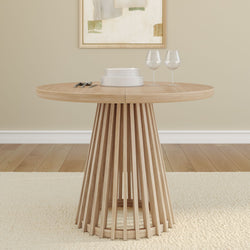 Round wooden dining table with modern slatted base, set with elegant white dishes and two wine glasses in a cozy dining room.