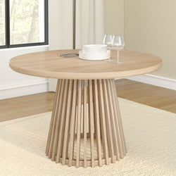 Modern round wooden dining table with glassware and plates in a bright room.