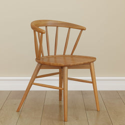 Wooden dining chair with curved backrest on hardwood floor in a minimalist room setting.