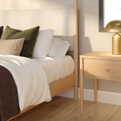 Scandinavian modern bedroom with light wood bed frame, white bedding, green textured pillows and wooden nightstand with gold lamp