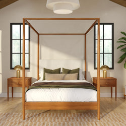 Modern wooden four-poster canopy bed in a bright neutral bedroom with green accent pillows, brass bedside lamps and black-framed windows
