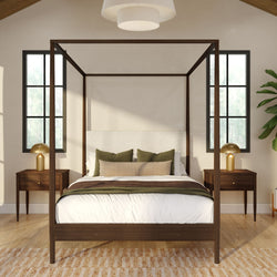 Modern bedroom interior with dark wood four-poster bed, white bedding and green accent pillows, matching wood nightstands with gold lamps, black-framed windows and hardwood floor