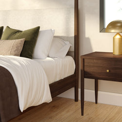 Modern minimalist bedroom with walnut wooden bed frame, crisp white bedding, green accent pillows, matching wooden nightstand and gold table lamp