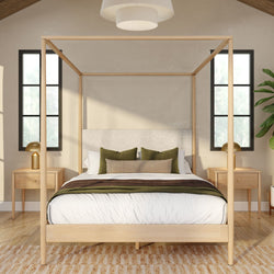 Modern minimalist master bedroom with light-wood four-poster canopy bed, white bedding and green accent pillows, matching wooden nightstands with gold lamps, black-framed windows, indoor plant, neutral palette and natural light on hardwood floor and area rug