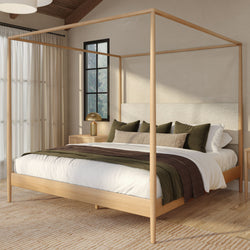 Wooden canopy four-poster bed in a cozy neutral modern bedroom with green and brown bedding, brass bedside lamp, black-framed window and sheer curtains