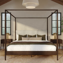 Modern wooden four-poster canopy bed in a neutral master bedroom with linen bedding, green accent pillows, brass bedside lamps, and black-framed windows