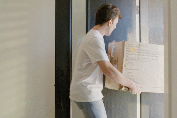 Man in white shirt carrying cardboard box into modern home entryway