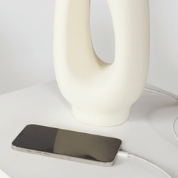Smartphone charging next to a modern ceramic vase on a white surface.